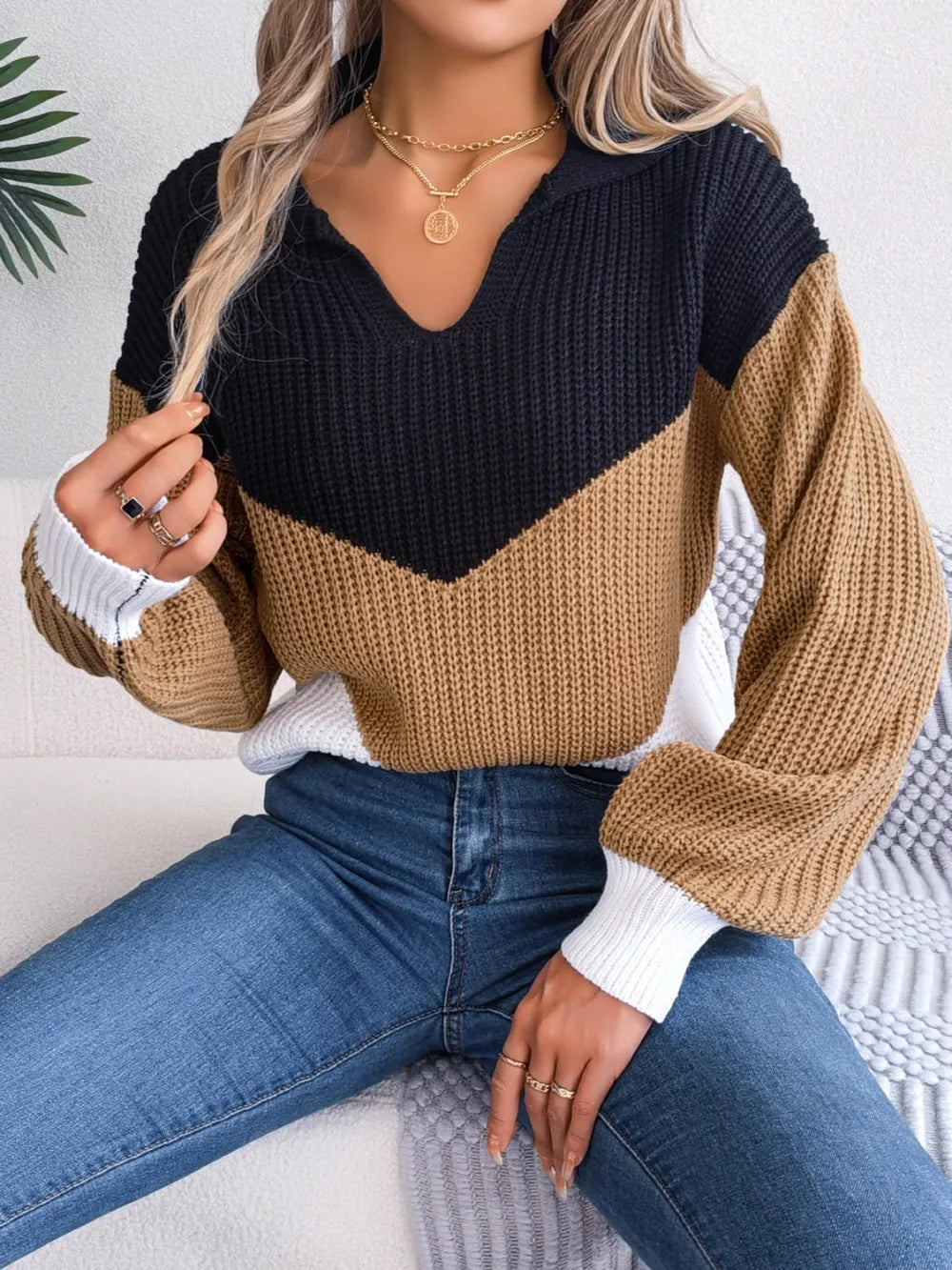 Woman wearing a color block dropped shoulder sweater in black, camel, and white, styled with blue jeans. Soft knit acrylic material.